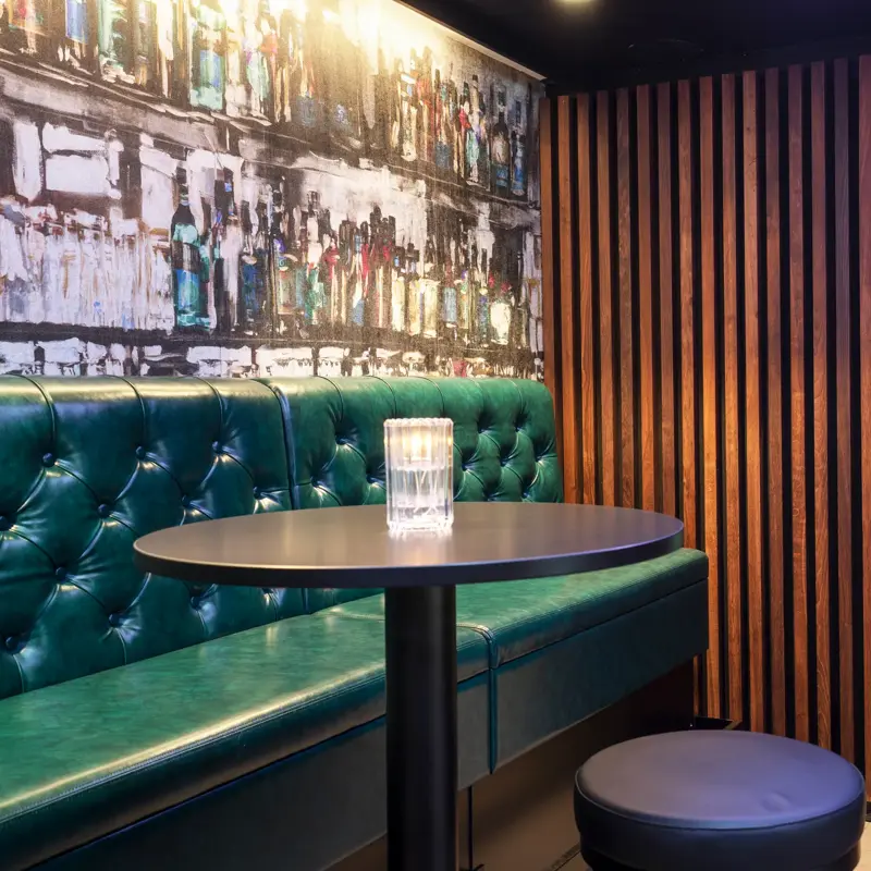 Svart rundt barbord, svart puff, grønn skinnsofa, grønn vegg, skillevegg i tre. 