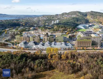 Illustrasjon viser et flyfoto av eksisterende Åsane sentrum, hvor nye planlagte bygninger er tegnet inn i grønt.
