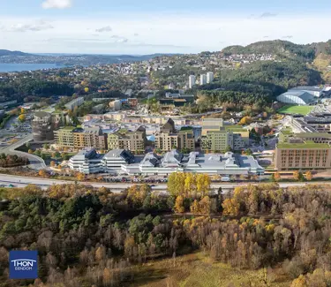 Illustrasjon viser et flyfoto av eksisterende Åsane sentrum, hvor nye planlagte bygninger er tegnet inn i grønt.