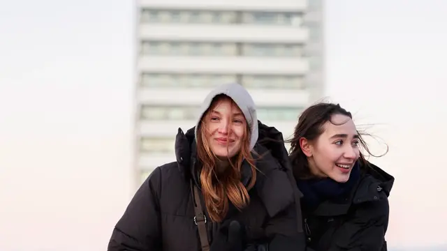 To jenter med store svarte boblejakker går i et bymiljø