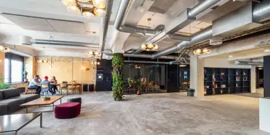 Stort oppholdsrom med store rør i taket og sittegrupper