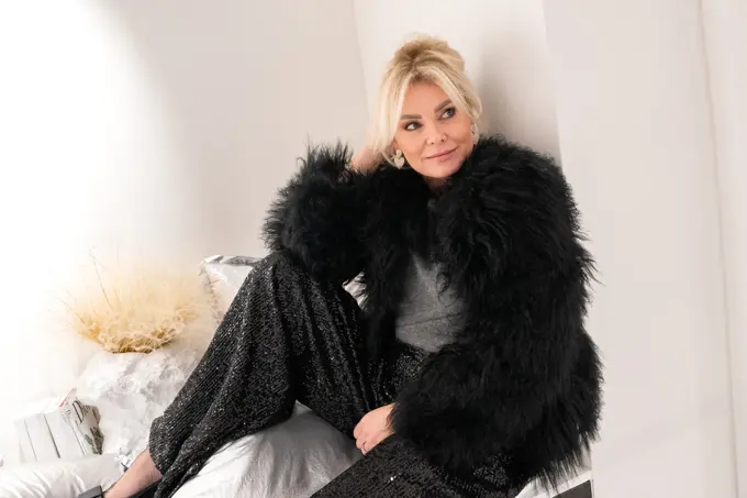 Dame med sort fuskepelsjakke, sølvtopp, glitrende bukser og pumps med sløyfe.