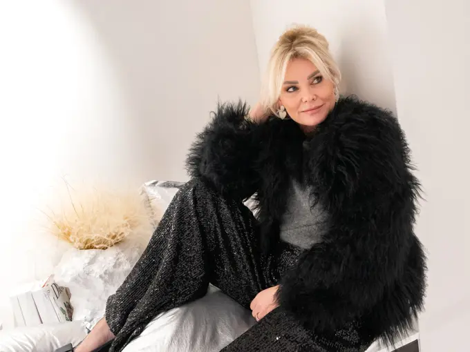 Dame med sort fuskepelsjakke, sølvtopp, glitrende bukser og pumps med sløyfe.