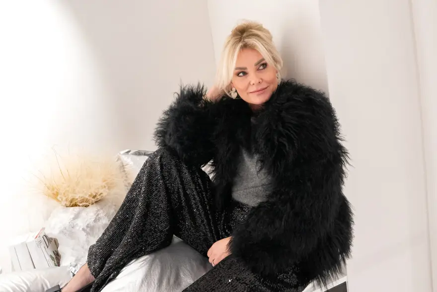 Dame med sort fuskepelsjakke, sølvtopp, glitrende bukser og pumps med sløyfe.
