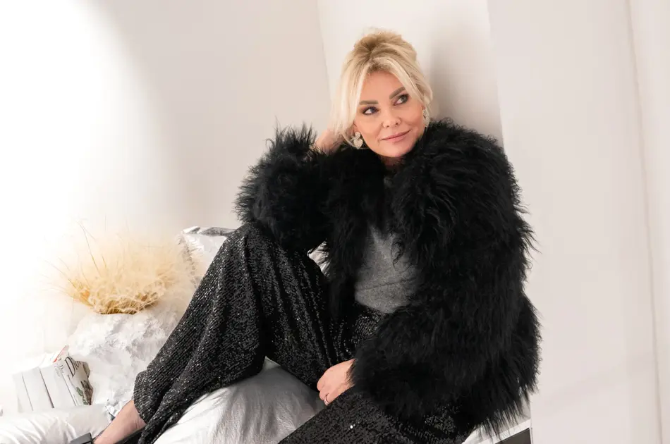 Dame med sort fuskepelsjakke, sølvtopp, glitrende bukser og pumps med sløyfe.