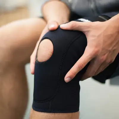 Nærbilde av kneet til en mann som holder på hver sin side av kneet sitt, som har knestøtte på