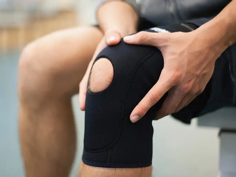 Nærbilde av kneet til en mann som holder på hver sin side av kneet sitt, som har knestøtte på