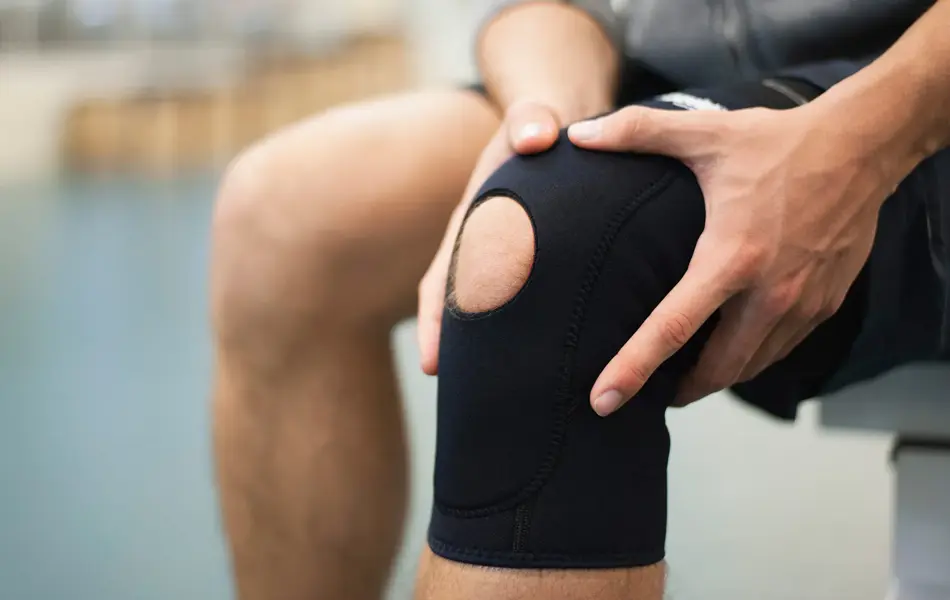 Nærbilde av kneet til en mann som holder på hver sin side av kneet sitt, som har knestøtte på