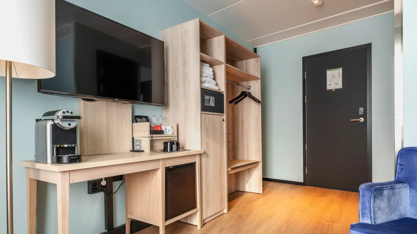 Junior suite med åpen garderobe ved inngangsdør, med avlangt bord ved siden av med nespresso maskin og veggehengt TV skjerm over. 