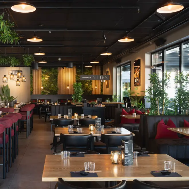 Oversiktsbilde av restauranten med flere bord, bar, grønne planter og hyggelig belysning