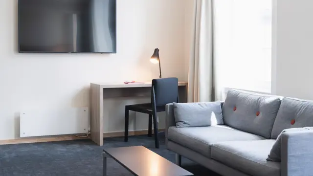 Suite med teppegulv, sofa, sofabord, skrivebord med stol og vegghengt TV.