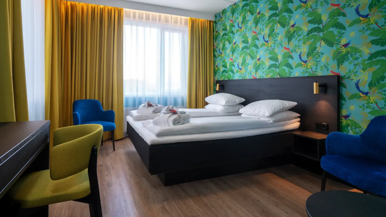 Grønn tapetvegg med mønster, gule gardiner, dobbeltseng, parkettgulv, blå stol, skrivebord, vindu, gul stol