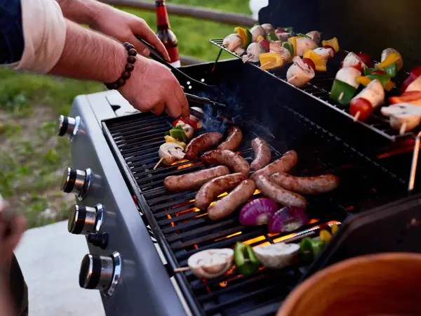 Chef cooking sausages and vegetables on skewers outdoors