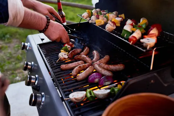 Chef cooking sausages and vegetables on skewers outdoors