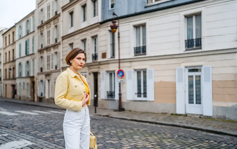 Dame med gul tweedjakke, hvit jeans og gul beske poserer på gate i Paris