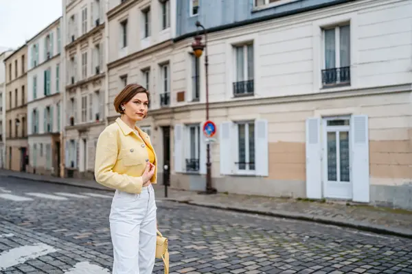 Dame med gul tweedjakke, hvit jeans og gul beske poserer på gate i Paris