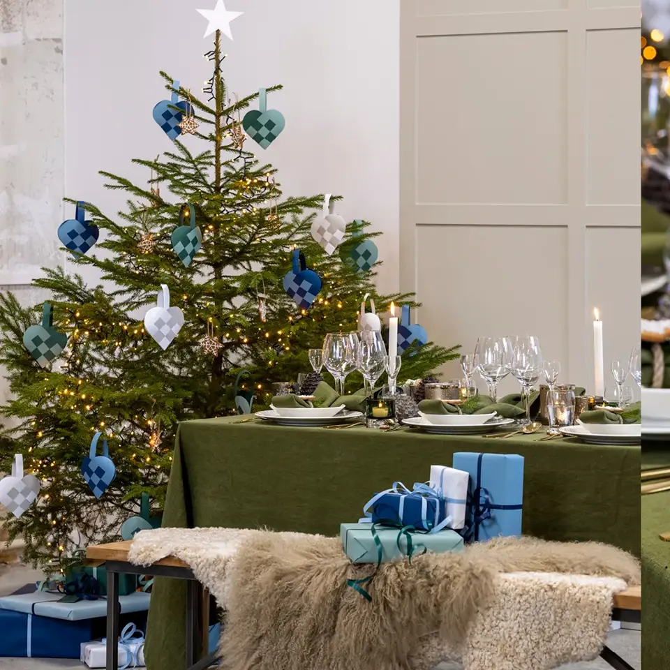 Dekket spisebord med juletre i bakgrunnen og nærbilde av kuvert på bordet.