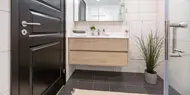 Bildet viser visningsleilighet på Høyfjellstunet på Skeikampen. Badet på bilde har mørkegråe fliser på gulvet, hvite fliser på veggene, speil, dusjhjørne med glassvegger og lyst tre på servantskapet.