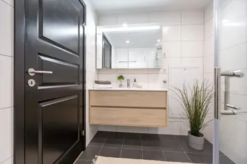 Bildet viser visningsleilighet på Høyfjellstunet på Skeikampen. Badet på bilde har mørkegråe fliser på gulvet, hvite fliser på veggene, speil, dusjhjørne med glassvegger og lyst tre på servantskapet.