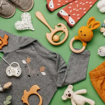 Illustrasjonsfoto til barnebutikk: Barneklær i gult, grått og blått, hvite joggesko, stripete lue, drikkeflaske og bamse på hvit bakgrunn.