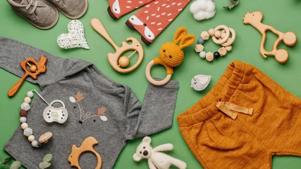 Illustrasjonsfoto til barnebutikk: Barneklær i gult, grått og blått, hvite joggesko, stripete lue, drikkeflaske og bamse på hvit bakgrunn.