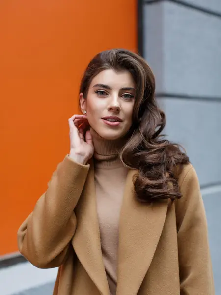 Dame med klassisk, beige kåpe og beige genser ser i kamera