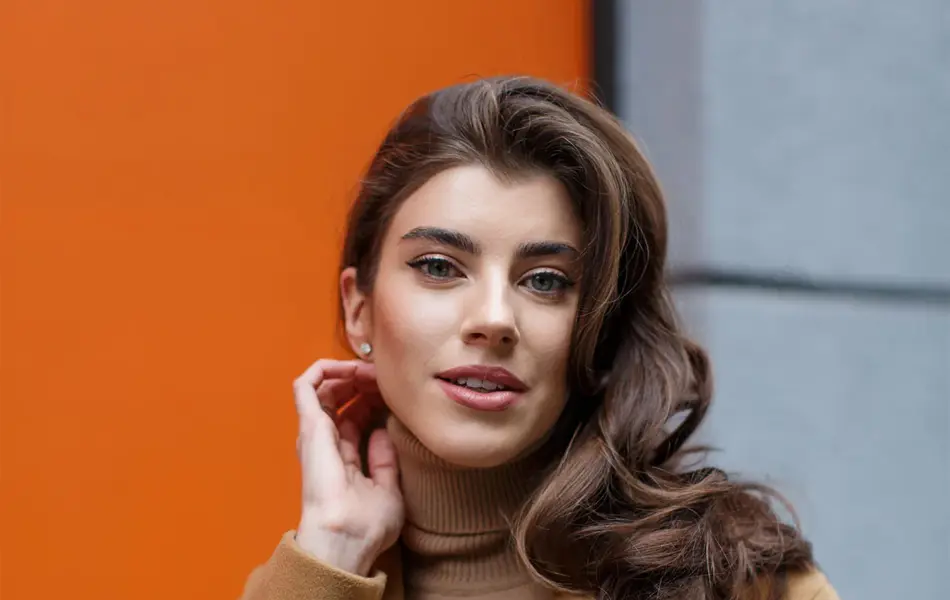 Dame med klassisk, beige kåpe og beige genser ser i kamera