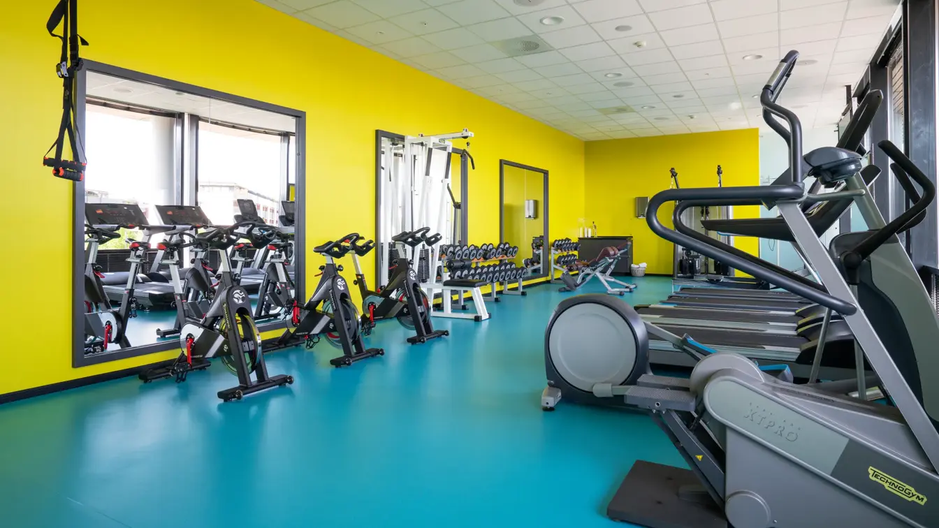 Diverse treningsapparater med gule vegger og turkisk gulv på treningsrom på Thon Hotel Arena i Lillestrøm