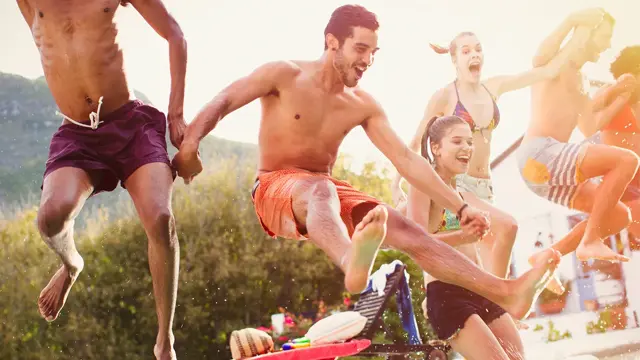 En gjeng unge mennesker hopper i basseng, nærmest en mann i burgunder badeshorts 