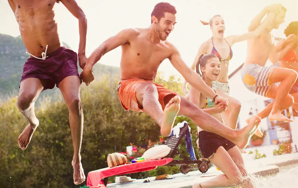 En gjeng unge mennesker hopper i basseng, nærmest en mann i burgunder badeshorts 