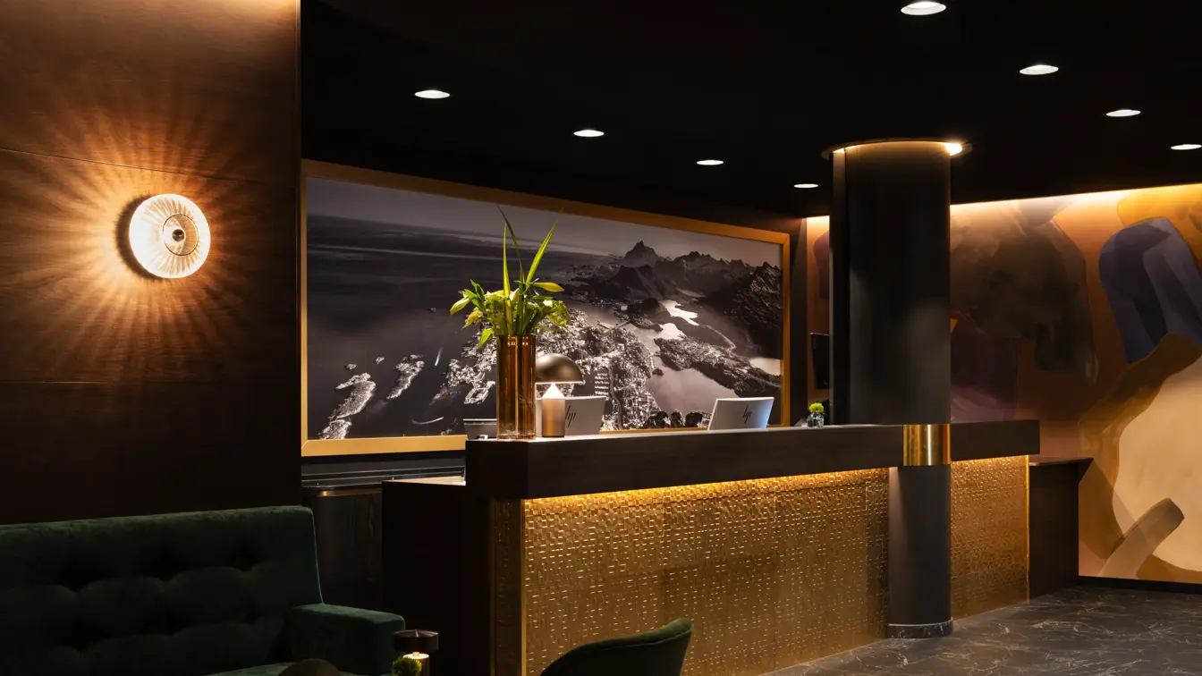 Gullfarget resepsjonsdisk, dempet belysning, svart tak med spotter, mørke fliser på gulvet