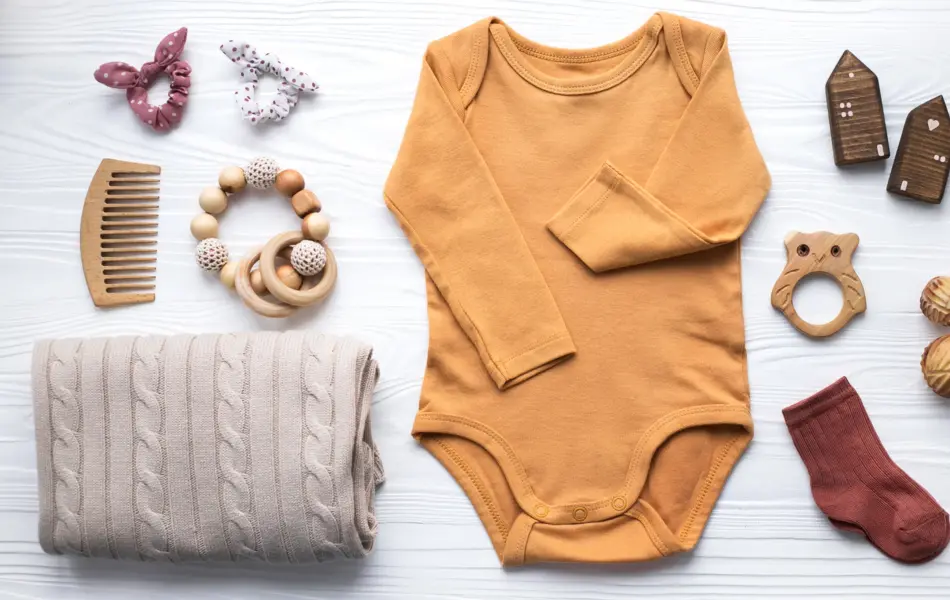 Newborn baby clothing, blanket, wooden toys, teether and accessories on white wooden background. Top view, flat lay.