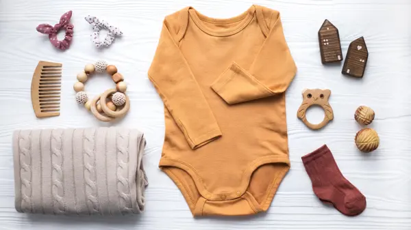 Newborn baby clothing, blanket, wooden toys, teether and accessories on white wooden background. Top view, flat lay.