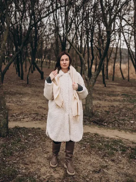 En dame med hvit fluffy jakke og brune boots går gjennom en park