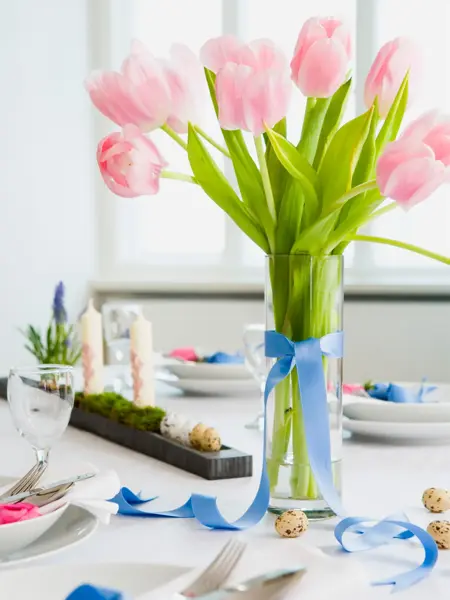 Vårbord med rosa tulipaner i en vase og en halvknytt sløyfe    