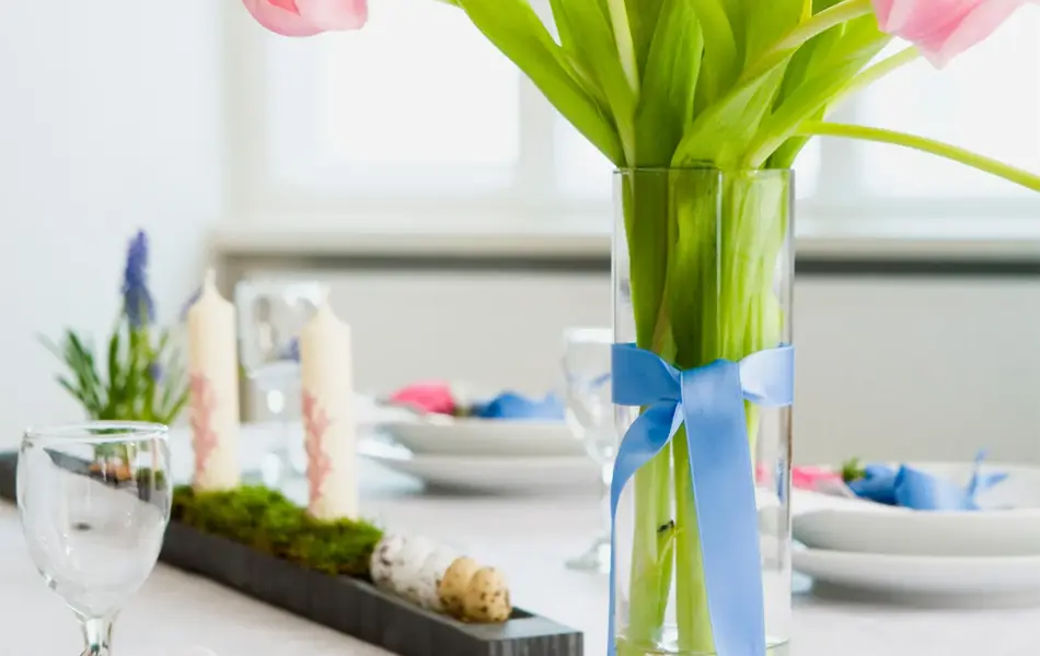 Vårbord med rosa tulipaner i en vase og en halvknytt sløyfe    