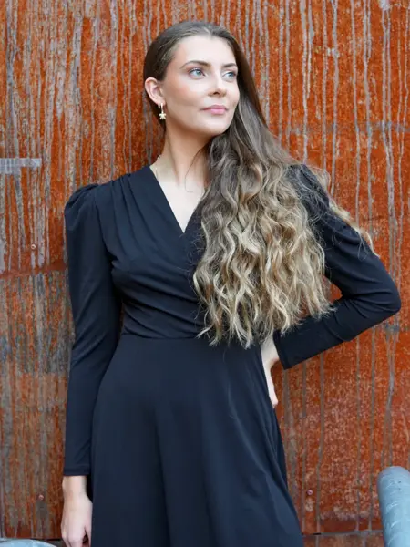 Dame med svart kjole og med rust vegg i bakgrunn