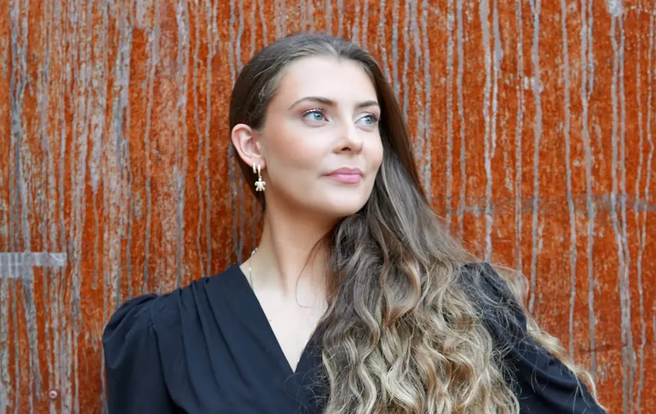 Dame med svart kjole og med rust vegg i bakgrunn