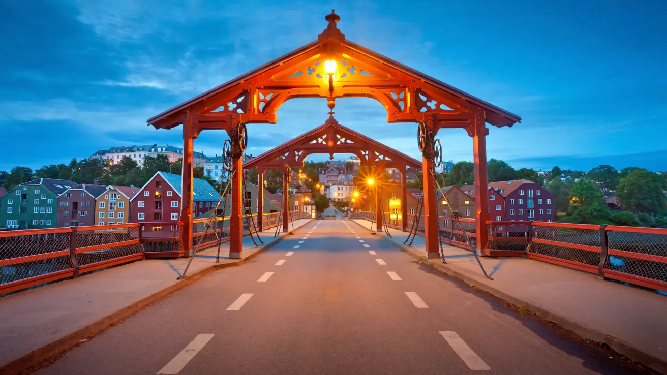 Bilde av Gamle Bybro i Trondheim. Asfaltert gangbro med to røde portaler i hver ende av broa. Rødt rekkverk på hver side. I bakgrunnen ses Bakklandet.