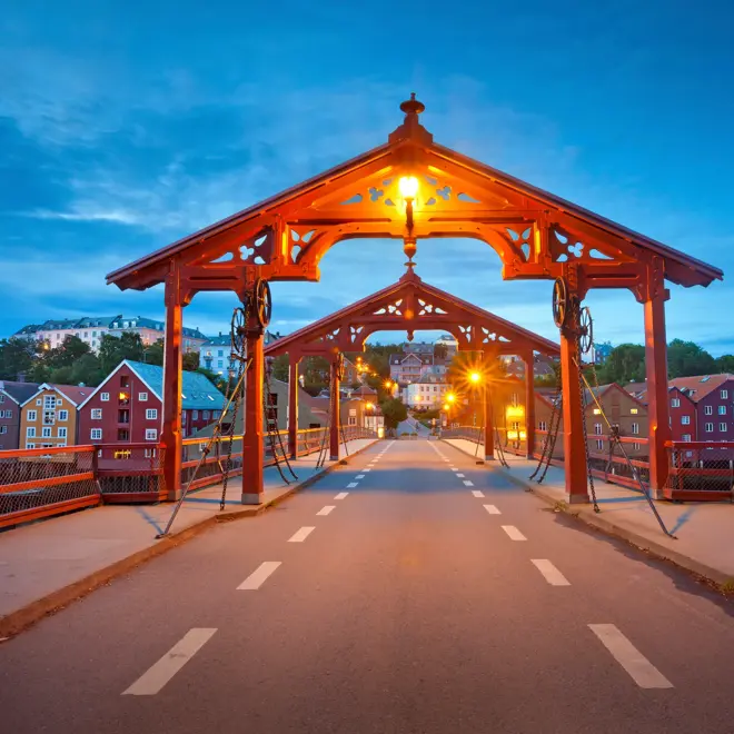 Bilde av Gamle Bybro i Trondheim. Asfaltert gangbro med to røde portaler i hver ende av broa. Rødt rekkverk på hver side. I bakgrunnen ses Bakklandet.