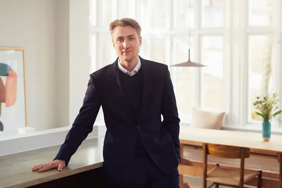 En mann som står og lener seg mot en benk i en leilighet