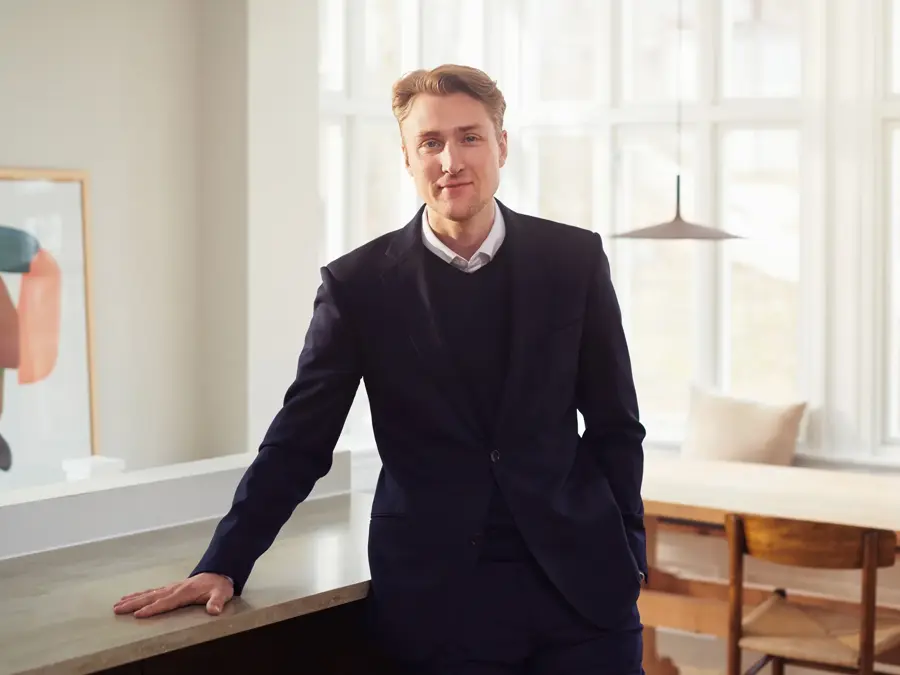 En mann som står og lener seg mot en benk i en leilighet