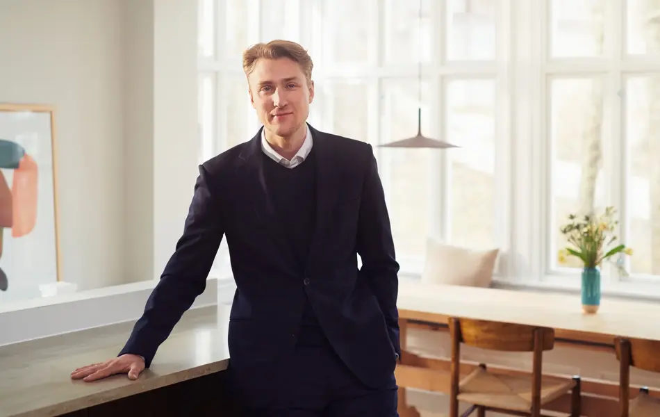 En mann som står og lener seg mot en benk i en leilighet