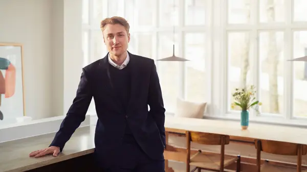 En mann som står og lener seg mot en benk i en leilighet