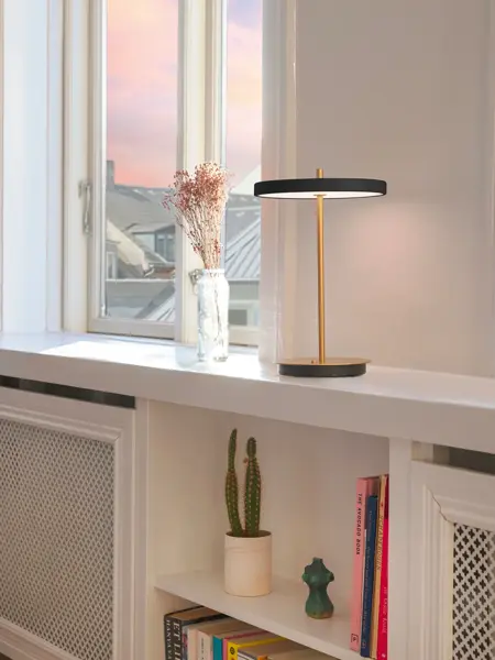 Sort bordlampe står på en hylle ved et vindu.