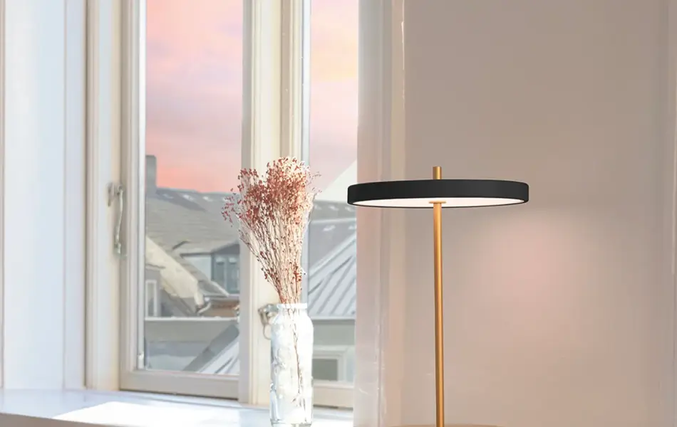 Sort bordlampe står på en hylle ved et vindu.