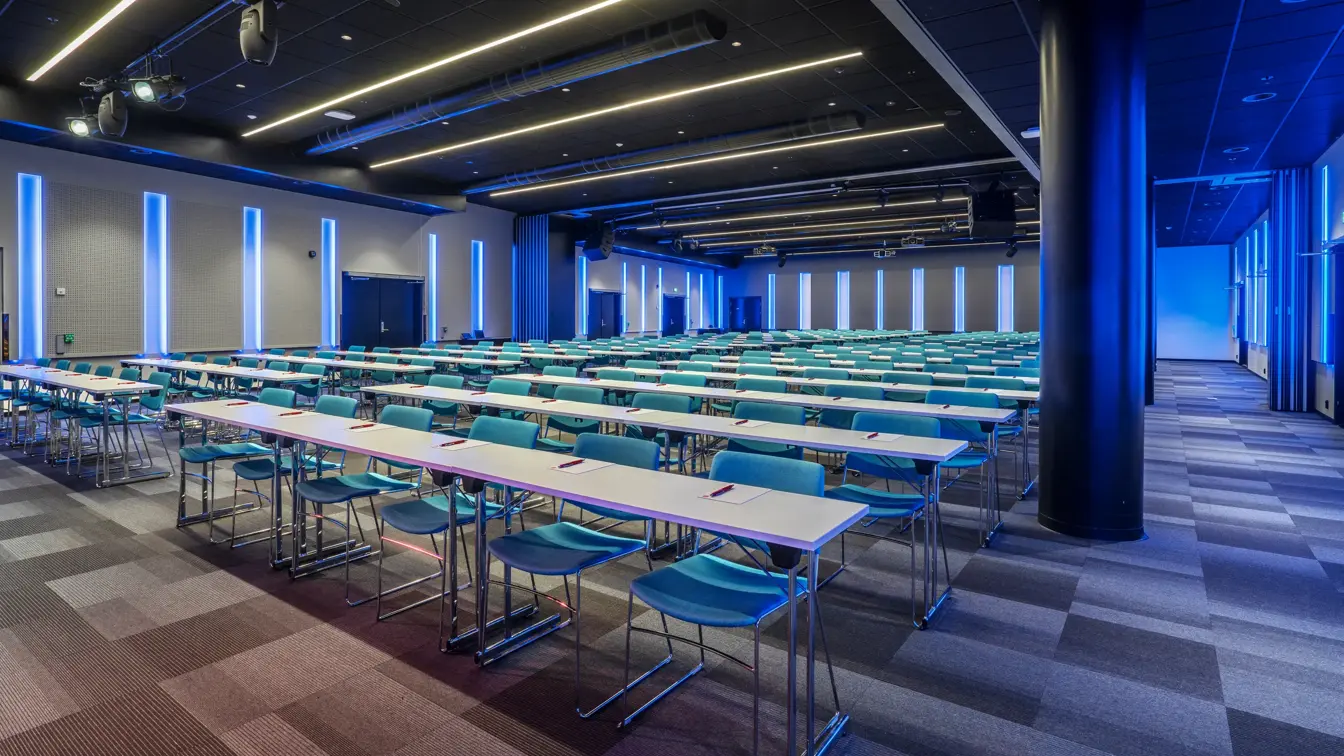 Storosalen hos Thon Hotel Storo, med klasseromsoppsett, blå belysning på vegger, lyskastere i taket og teppebelagt gulv.