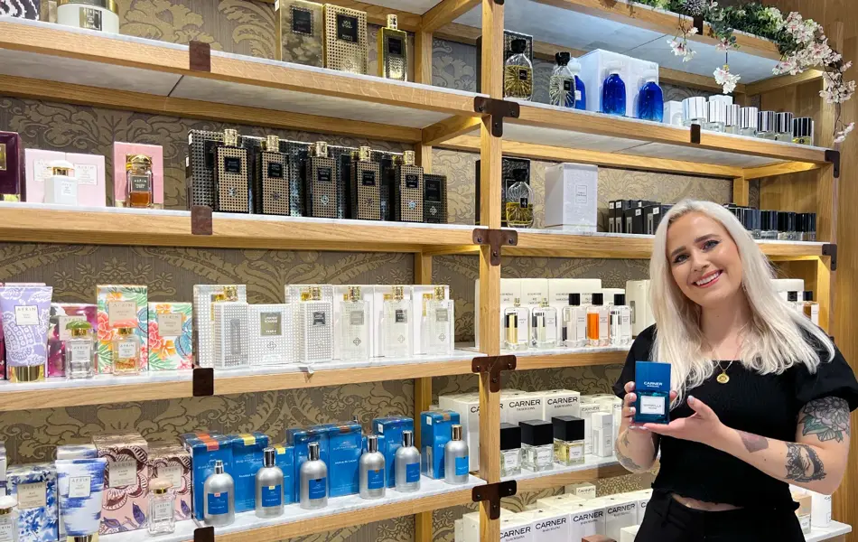 Kvinnelig butikkansatt på Fredrik & Louisa holder en parfyme foran en hylle med produkter