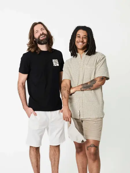 To menn i sort t-skjorte, hvit shorts og rutete skjorte og beige shorts.