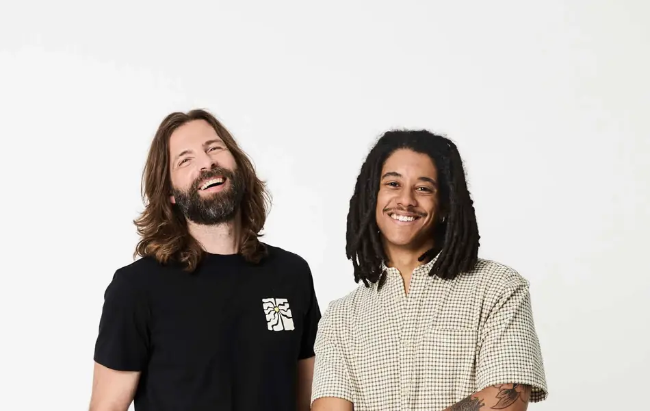 To menn i sort t-skjorte, hvit shorts og rutete skjorte og beige shorts.